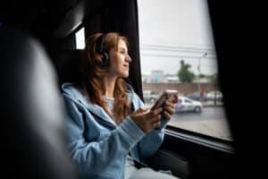 Young woman holding mobile phone and looking through window on travel bus