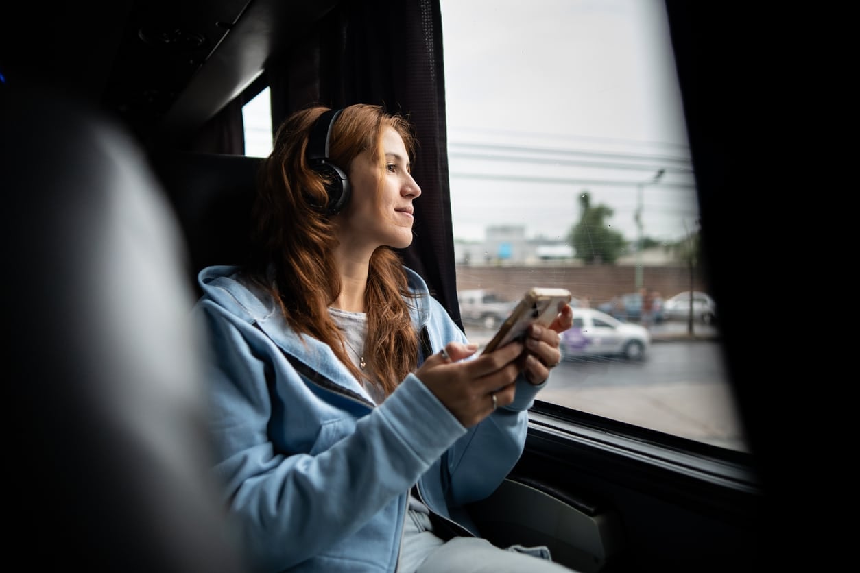 Young woman holding mobile phone and looking through window on travel bus